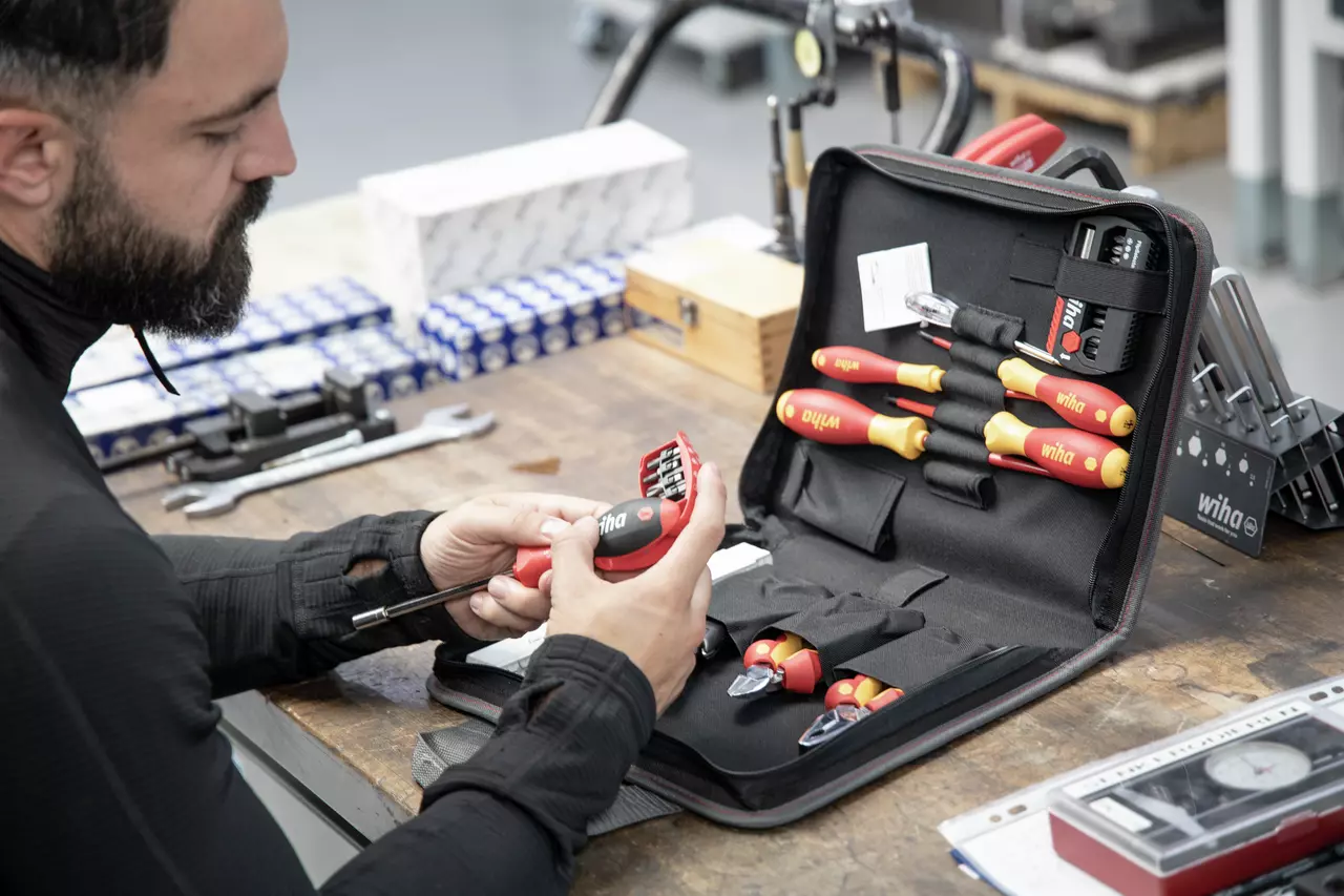 A person examining a tool set with insulated screwdrivers and a bit holder on a workbench.