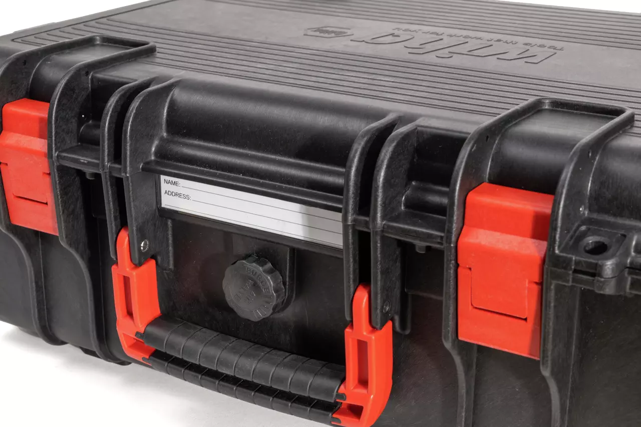 Black protective case with red latches and a handle, featuring a label for name and address.