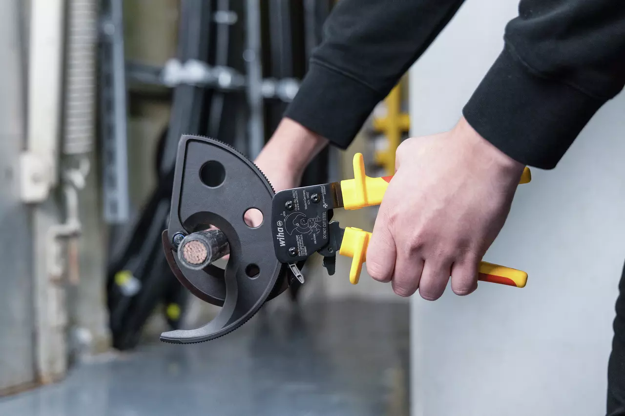 Person using ratchet cable cutter with yellow handles to cut a thick cable.