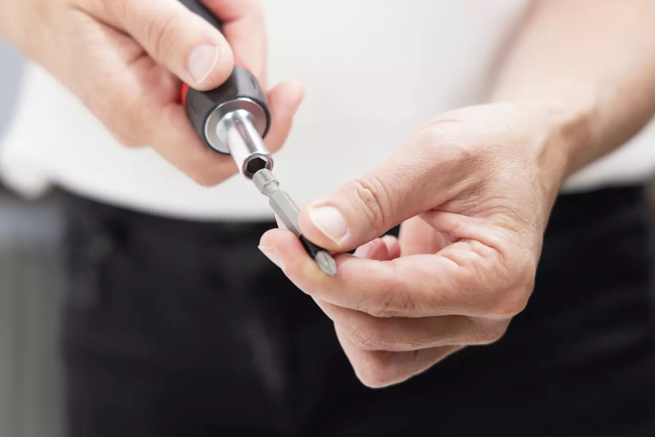 Person inserting a bit into a black and red screwdriver handle